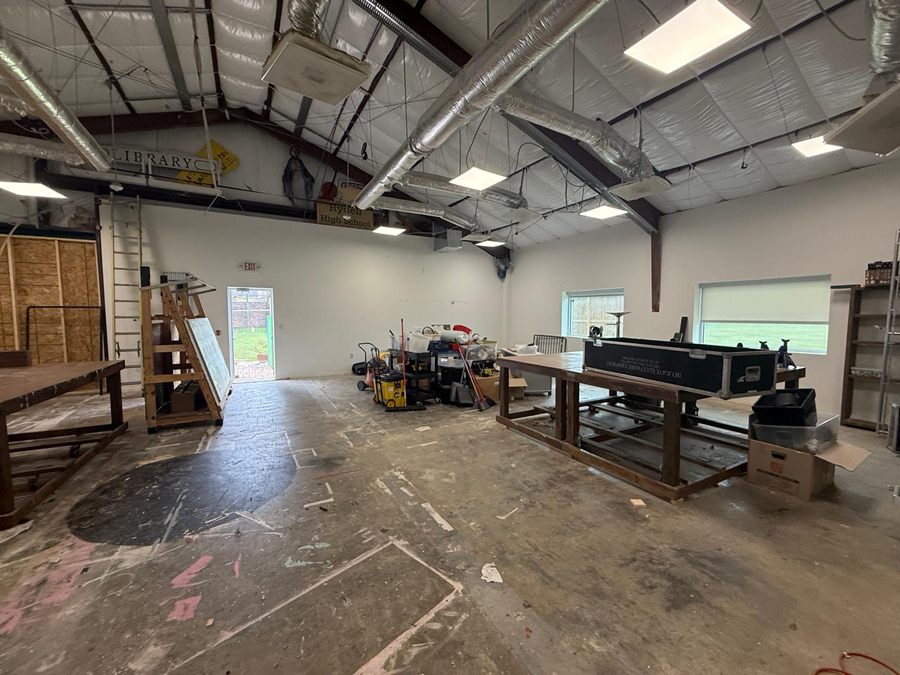 Before: the workshop as found, crowded with worktables, stored equipment and old signage under the exposed steel frame
