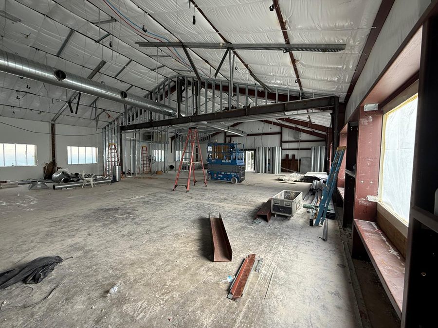 Construction: a steel beam spans the room with new metal-stud framing above it, a scissor lift and ladders below