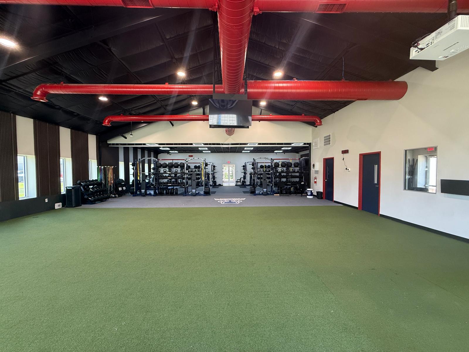 The turf hall end to end under the red ductwork, the weight room beyond