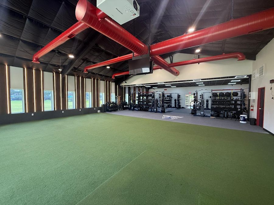 The window wall of the turf hall, slatted panels lit between each window, red ducts overhead
