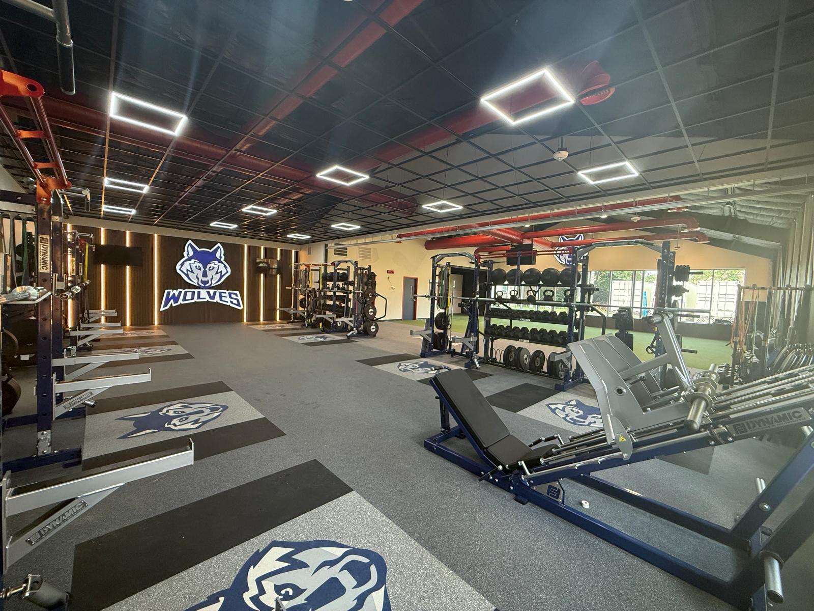St. Francis Episcopal School, Houston - weight room with racks and lifting platforms, the lit Wolves wall at the far end